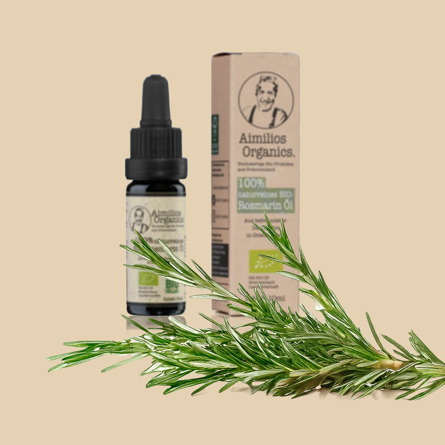 Aimilios Organics Bio Rosmarin Öl auf braunem Hintergrund mit Rosmarin Pflanzen im Vordergrund